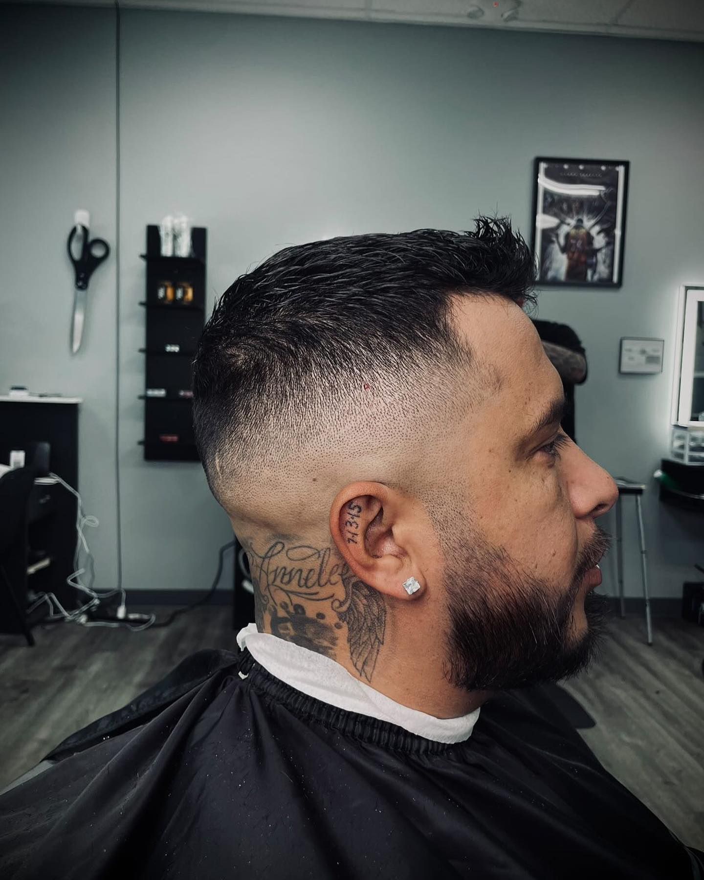 Man with a faded haircut, beard, and neck tattoo in a barbershop.