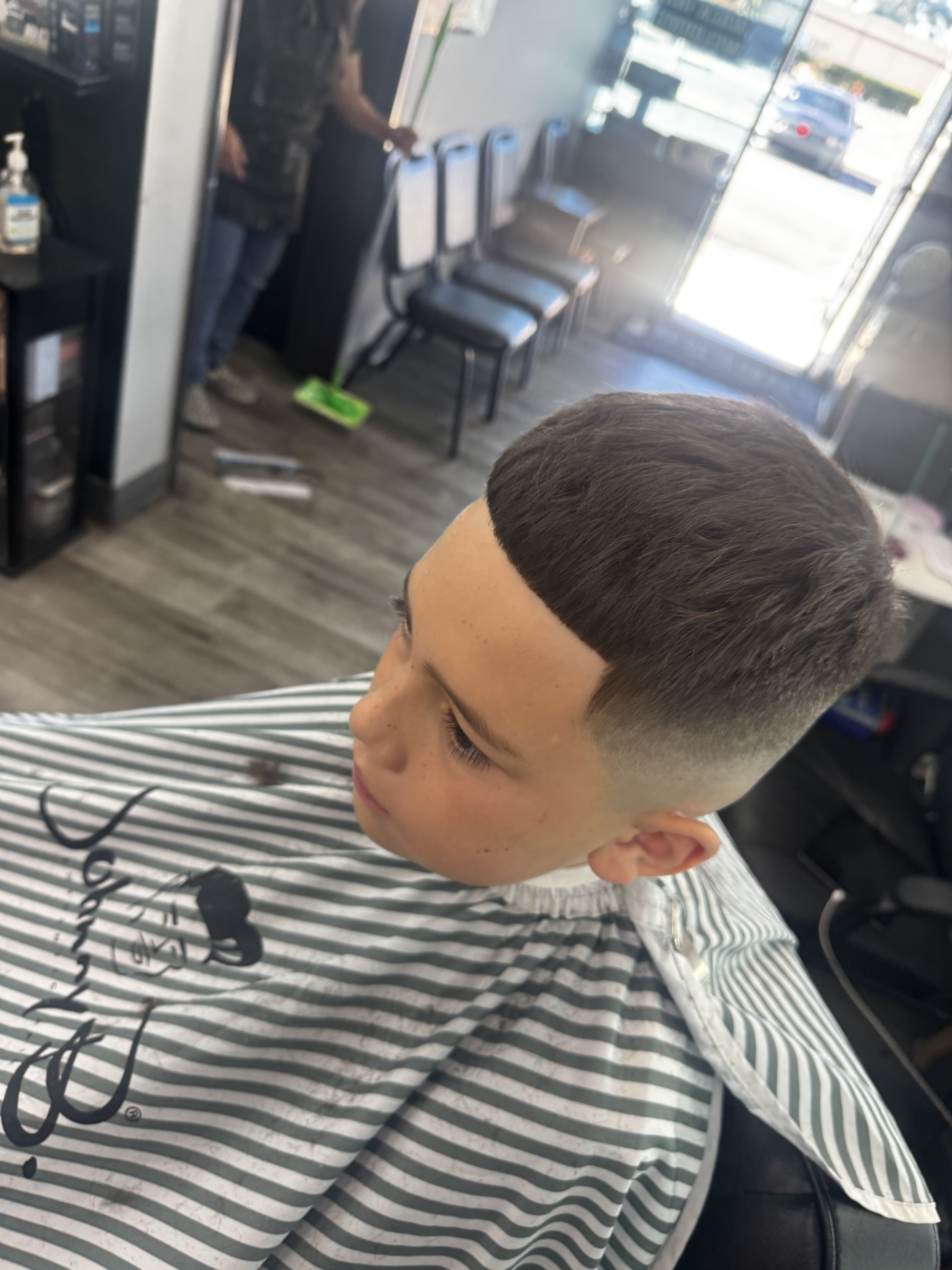 Boy getting a haircut at a barbershop; faded sides, bowl-cut style.