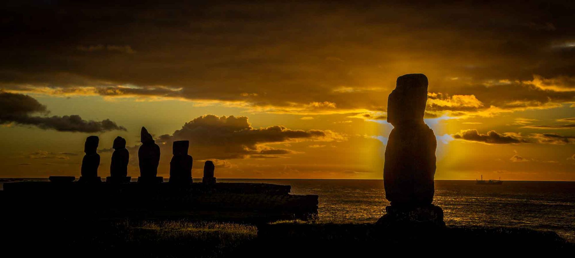 A group of statues standing next to each other on a beach at sunset.