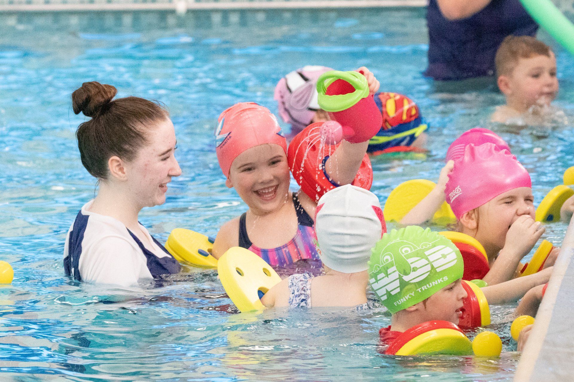 A group of children are swimming in a pool with a teacher.