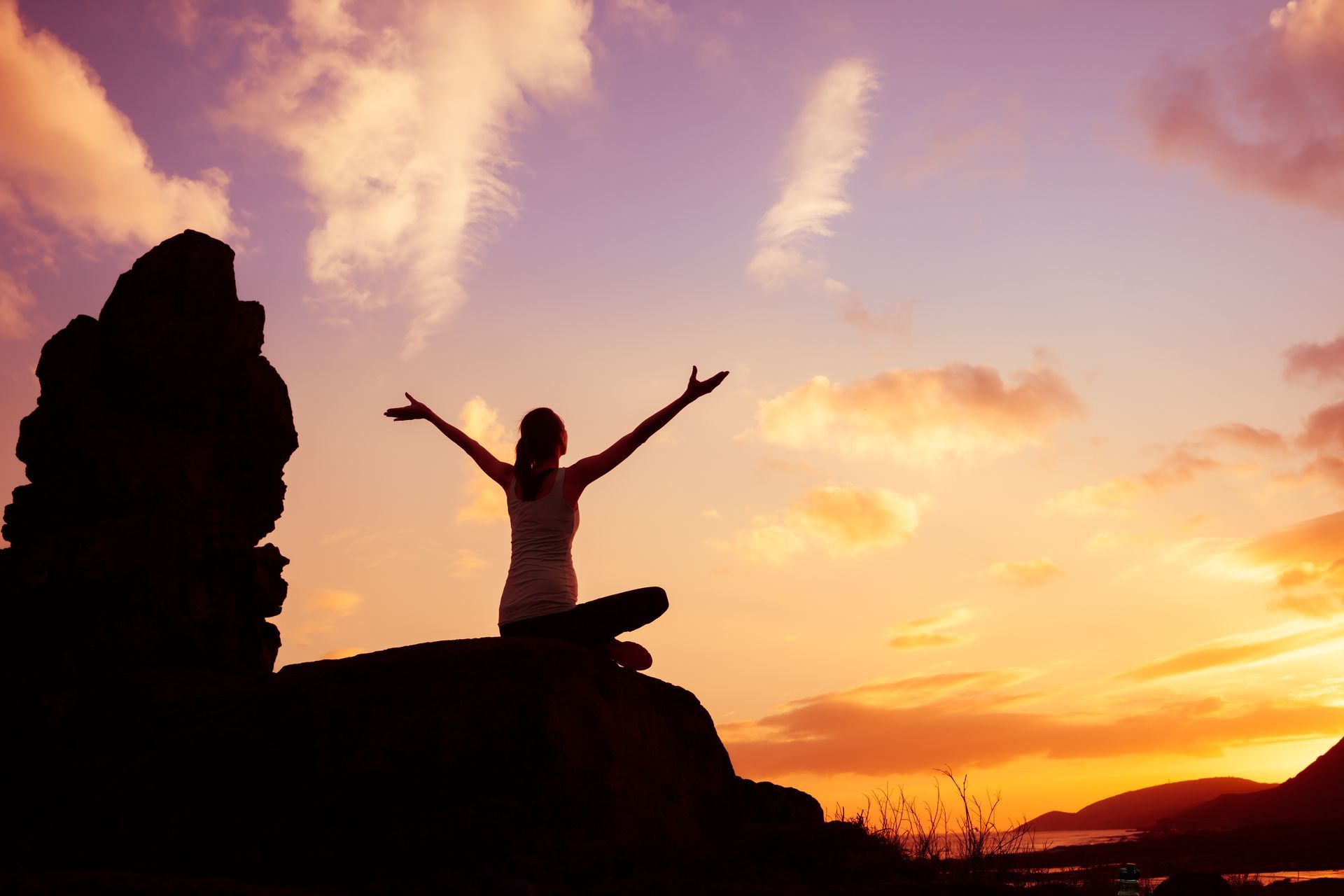Silhouette of Person With Arms Raised, Seated on Rocks at Sunset — Wide Bay Chiropractic in Gympie, QLD