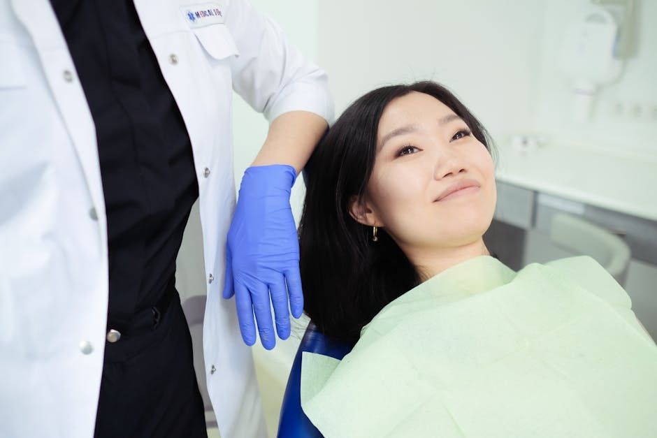 Patient reclining in a dental chair while a clinician in a white coat and blue gloves stands nearby