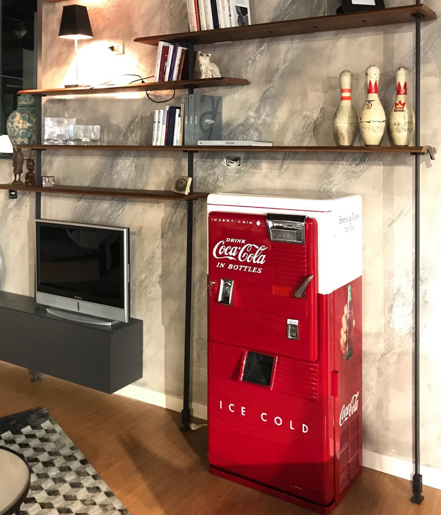 Soggiorno con distributore automatico di Coca-Cola, scaffali, TV e birilli.
