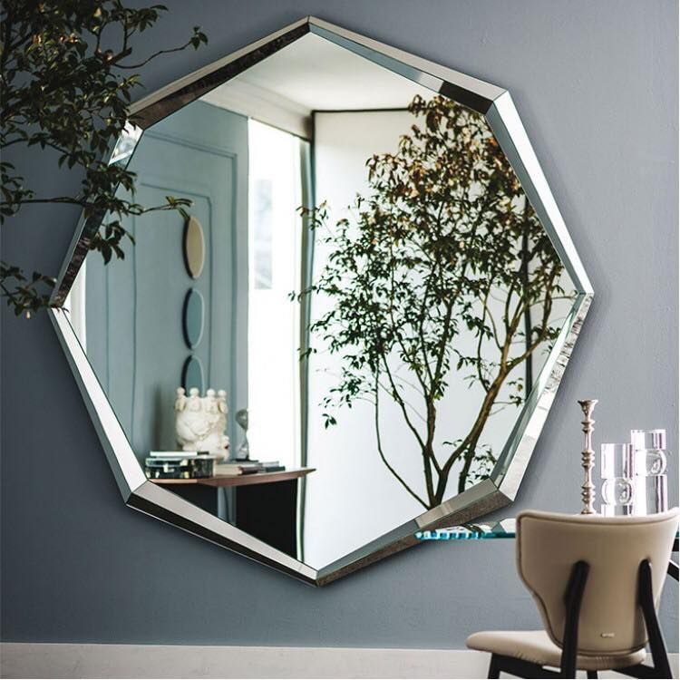 Grande specchio sfaccettato che riflette una stanza con un albero visibile attraverso una porta.
