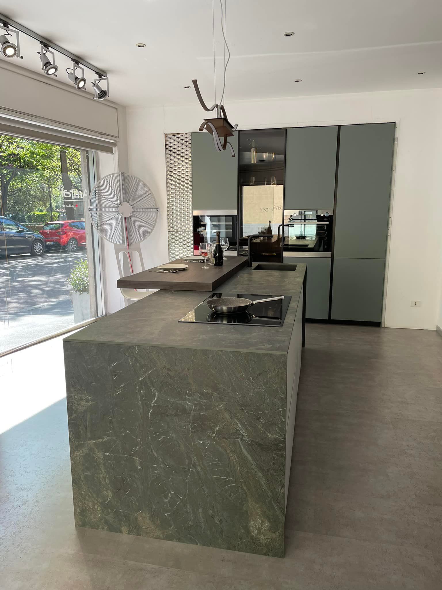 Cucina moderna con isola in pietra verde scuro, mobili grigi e vista sulla strada.