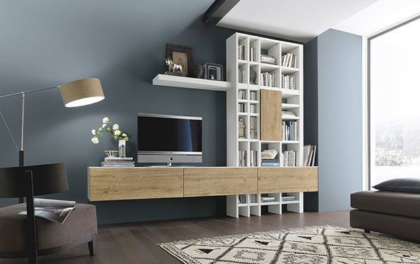 Soggiorno moderno con pareti blu, mobile porta TV in legno chiaro e libreria bianca.