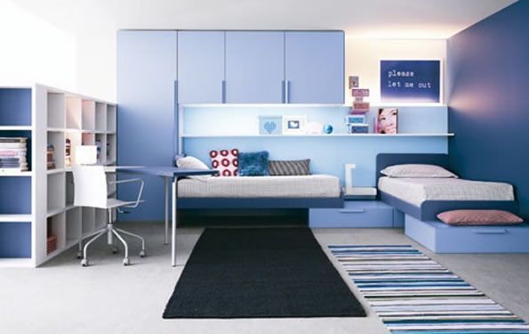Camera da letto moderna blu e bianca con scrivania, letti a muro, contenitori e scaffali.