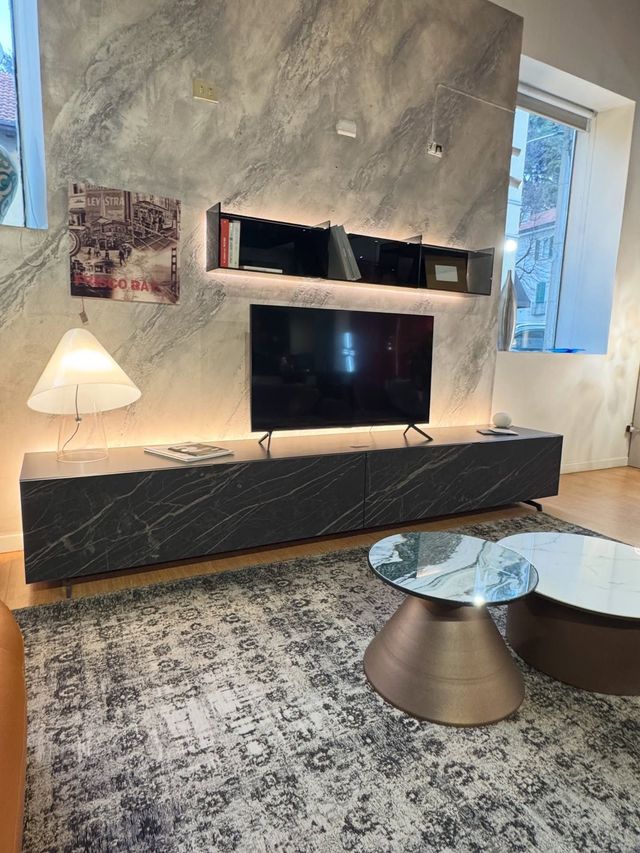 Soggiorno moderno con mobile TV effetto marmo grigio, televisore e tavolini da caffè su un tappeto a fantasia.