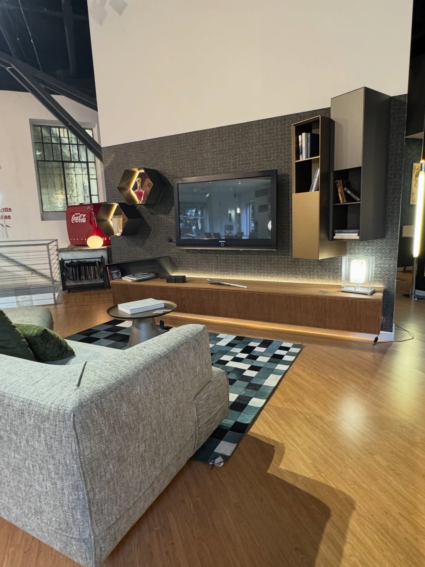 Soggiorno moderno con TV, mensole sospese, mobile in legno, divano grigio e tappeto geometrico.