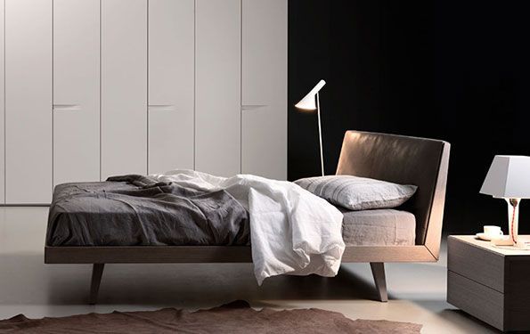 Camera da letto con letto sfatto, comodino con lampada, lampada da terra contro la parete nera e armadio.