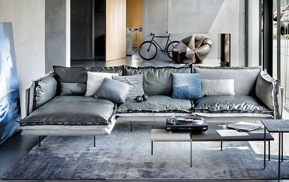 Soggiorno moderno con divano componibile grigio, tavolini bassi e tappeto. Bicicletta e opere d'arte visibili sullo sfondo.