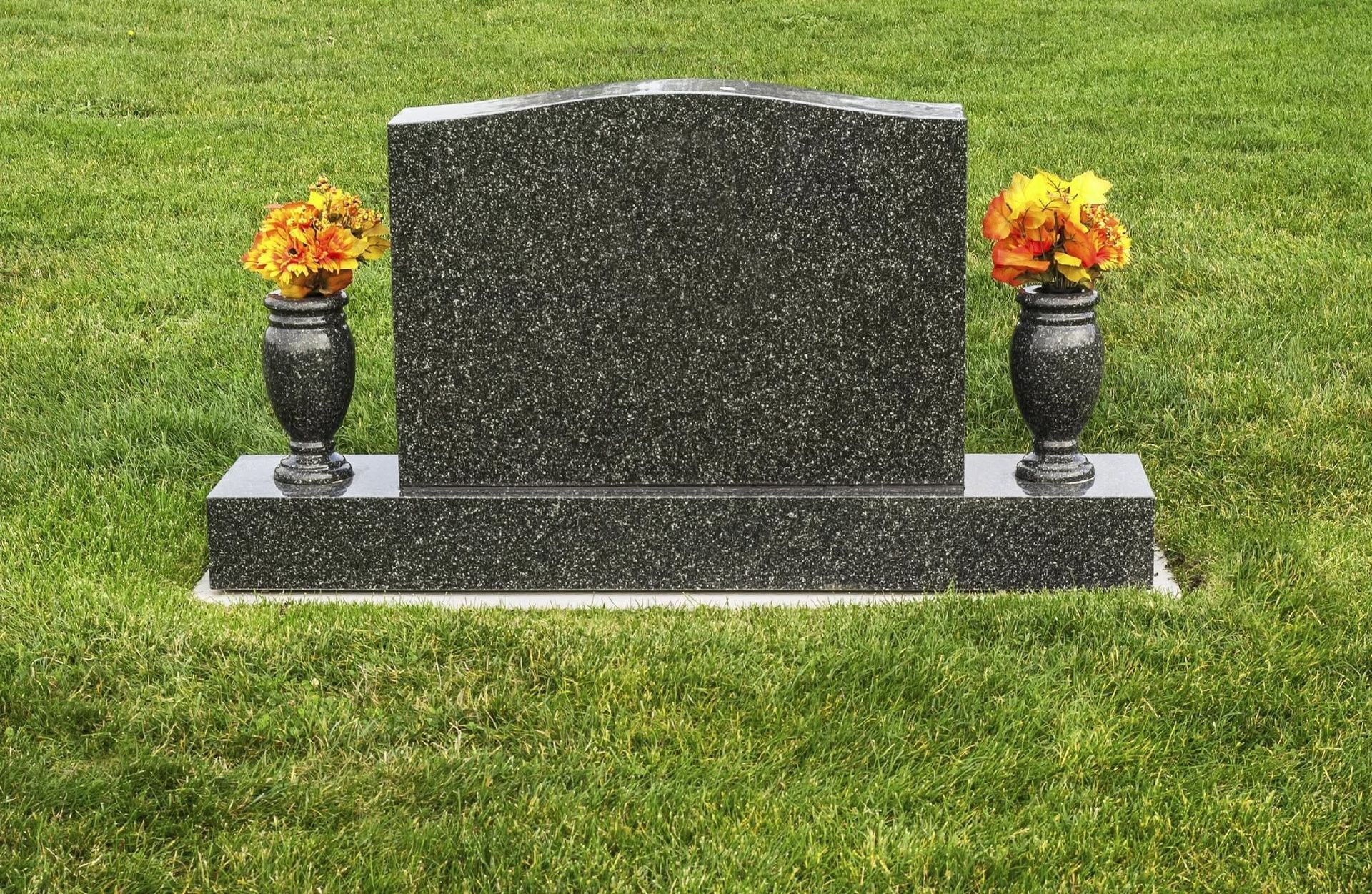 Gravestone with two flower vases on either side in a grassy cemetery