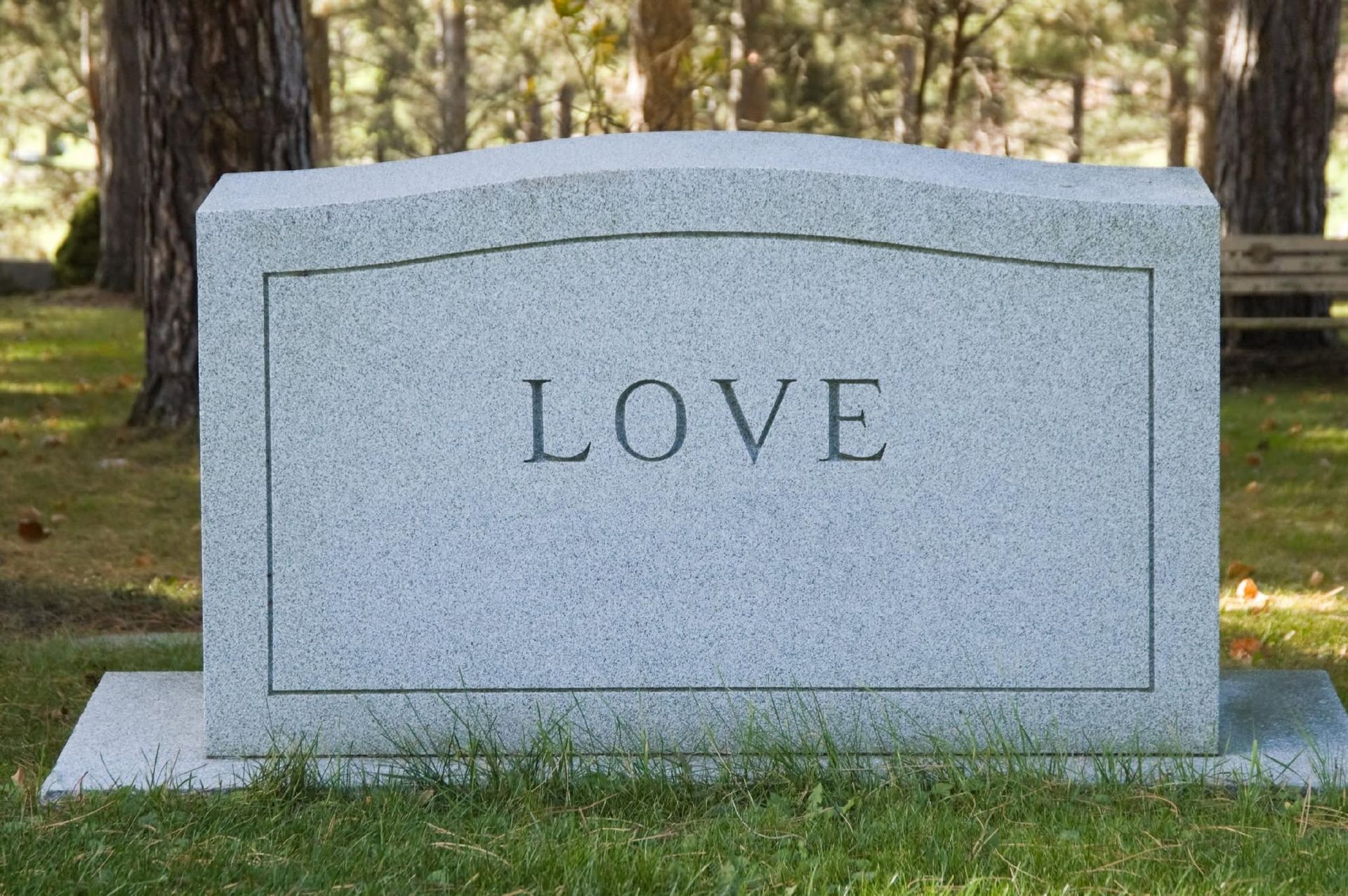 Gray granite gravestone engraved with the word “LOVE” in a grassy cemetery.
