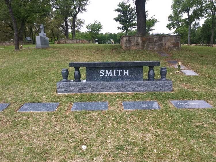 Smith gravestone in a grassy cemetery, with small memorial plaques in front and trees behind.