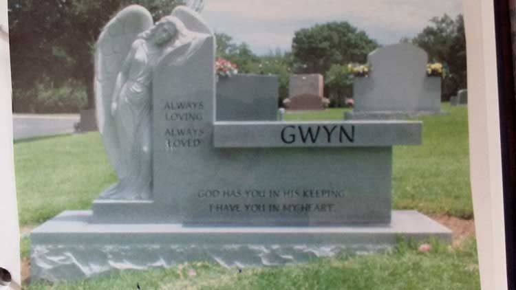 Gravestone monument with the name GWYN in a green cemetery lawn, with two carved figures on the left.
