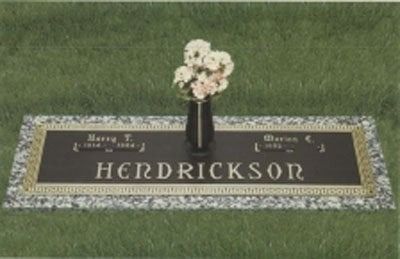 Grave marker with “Hendrickson” engraved, bordered in stone and topped with a vase of flowers.