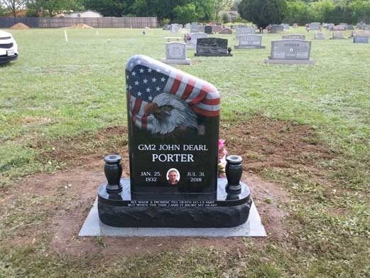 Black granite memorial headstone with American flag engraving in a grassy cemetery