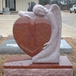 Stone angel hugging a large red heart-shaped monument on a pedestal outdoors