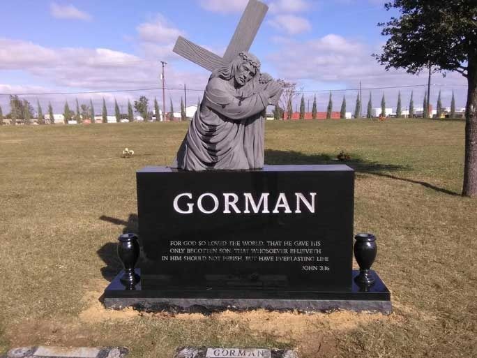 Gorman cemetery monument with a soldier statue carrying a cross on a black base in a grassy field