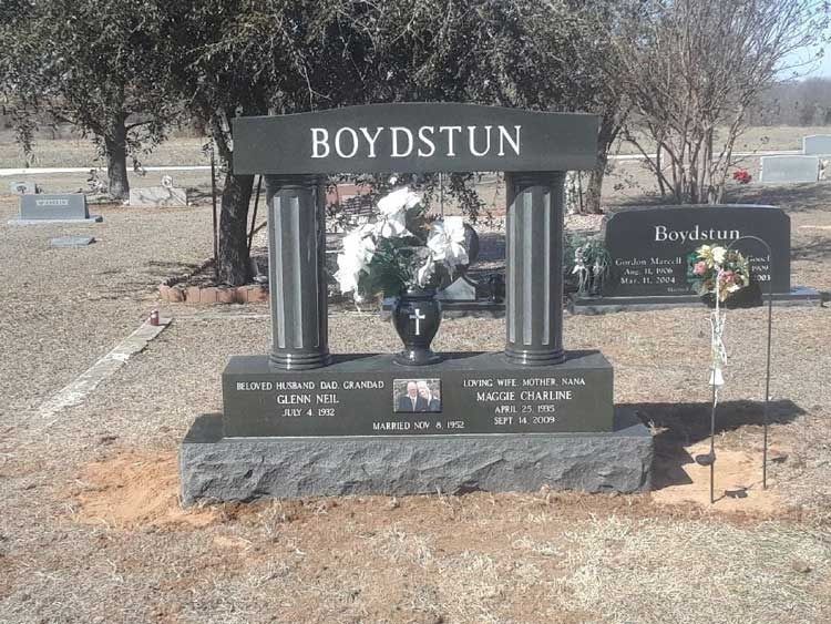 Boydstun memorial headstone with vase and flowers in a cemetery, topped with a cross.