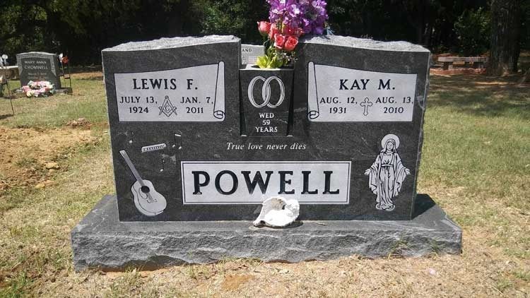 Black granite gravestone with photos, flowers, and the name POWELL in a cemetery.