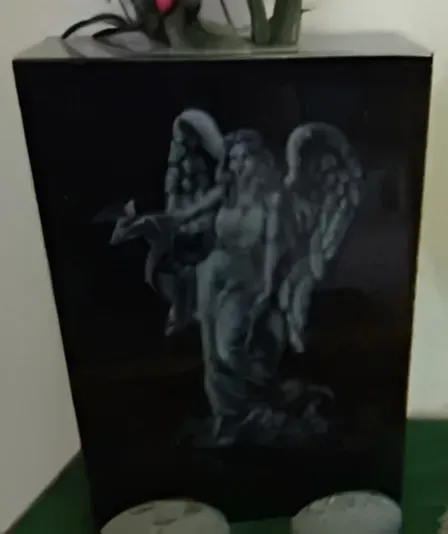 Black box with a gray angel statue on the front, displayed indoors on a green surface.