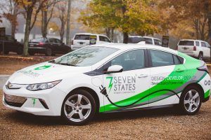 A white and green electric car is charging in a parking lot.