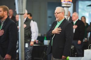 A man in a suit and green shirt is standing in front of a crowd of people.