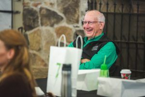 A man in a green vest is smiling while sitting at a table.