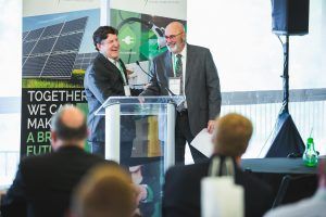 Two men are standing at a podium giving a presentation to a group of people.