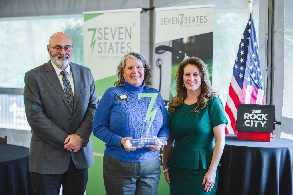 Three people are standing next to each other in front of a sign that says seven states.