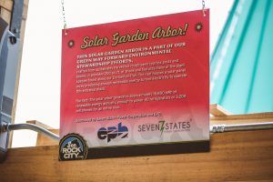 A sign that says solar garden arbor is hanging from a metal pole.