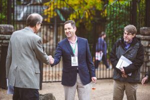 Three men are shaking hands in front of a fence.