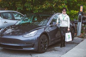 A woman is standing next to a tesla model 3 at a charging station.