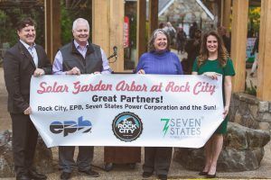 A group of people are holding a banner that says solar garden arbor at rock city.