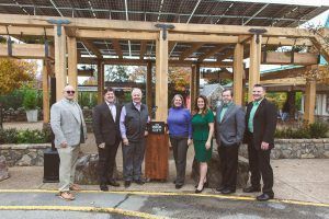 A group of people are standing in front of a wooden structure.