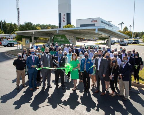 A group of people are cutting a green ribbon in front of a rocket.