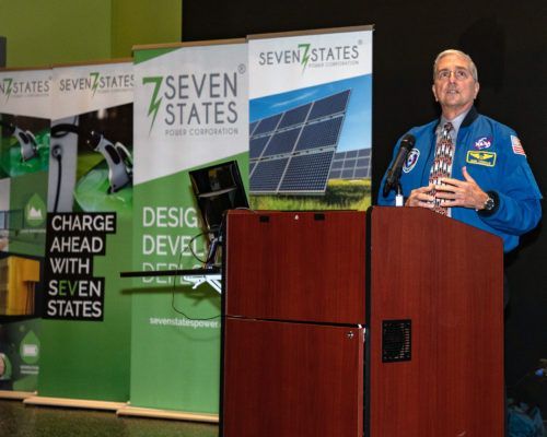 A man is standing at a podium in front of a sign that says seven states