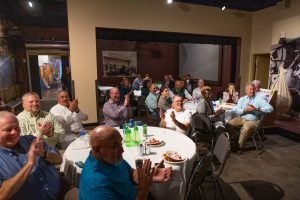 A group of people are sitting at tables in a room applauding.