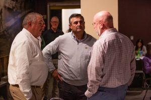 Three men are standing next to each other and talking in a room.