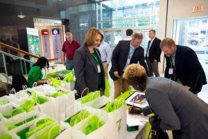 A group of people are standing around a table with green bags.