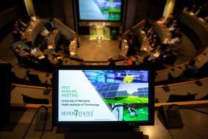 A group of people are sitting in an auditorium watching a presentation on a large screen.