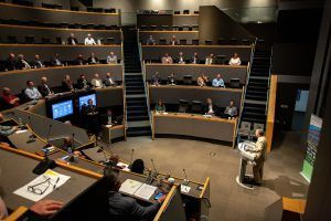 A man is giving a presentation in front of a large audience in a lecture hall.