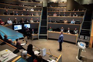A man is giving a presentation in front of a large audience in a lecture hall.