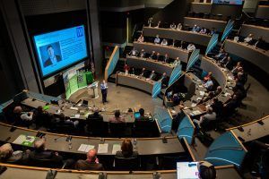 A man is giving a presentation in front of a large audience in a lecture hall.