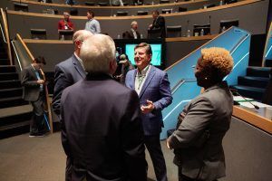 A group of people are standing in an auditorium talking to each other.