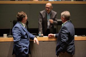 Three men in suits are talking to each other in a conference room.