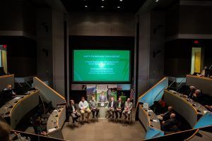 A group of people are sitting in front of a large screen in a conference room.