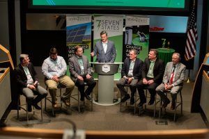 A group of men are sitting around a podium in a conference room.
