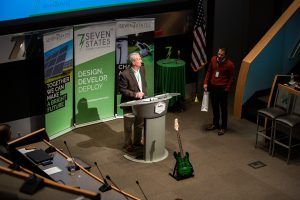A man is standing at a podium with a guitar in front of him.
